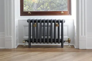 A plain Mercury 4 column cast iron radiator in a dark grey sparkle finish on feet, with brass valves and stays, beneath a sash window.