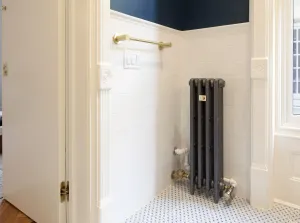 Narrow Mercury 4 column cast iron radiator in mid grey sparkle on feet, beside white metro tiles, a mosaic floor and a brass towel rail.