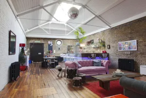 Two ornate Rococo III cast iron radiators in Charcoal on brick walls of an open-plan loft with wooden floor, pink sofa and bar.