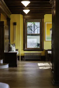 A low plain Mercury cast iron radiator in Bronze Gold under a leaded window, set in a yellow room with dark oak panelling and herringbone floor.