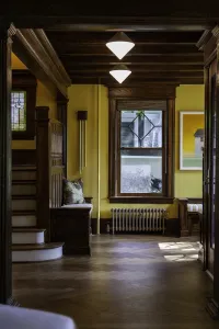 Low plain Mercury 4 Column cast iron radiator in Bronze Gold under a window in a yellow hallway with dark oak beams and herringbone floor.