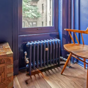 Mercury 4 Column 460mm cast iron radiator in Farrow & Ball Serge under a window, with a brass valve, wall stay and a wooden chair.