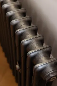 Close-up looking down the top of a plain Mercury 3 Column cast iron radiator in Natural Pewter against a pale wall above a wooden floor.