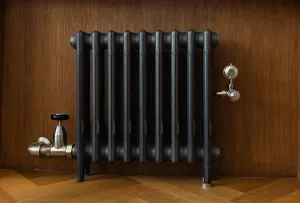 Mercury 3 Column cast iron radiator in Natural Pewter on feet against oak panelling, with a nickel angled valve and lockshield, on a herringbone floor.