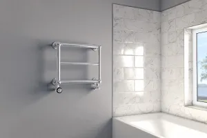 Elara wall-mounted chrome towel rail with three bars and angled valves on a grey wall beside a marble-tiled bath and window.