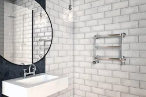 Elara three-bar towel rail in polished chrome with valves, wall-hung on white brick tiles beside a stone basin and round mirror.