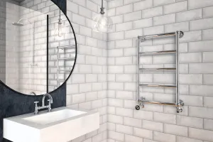 Wall-hung Elara towel rail in chrome with five bars and angled valves on white brick tiles, beside a basin, round mirror and pendant light.