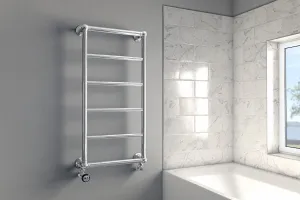Wall-hung Elara chrome towel rail with six bars and angled valves on a grey wall beside a marble-tiled bath alcove and window.