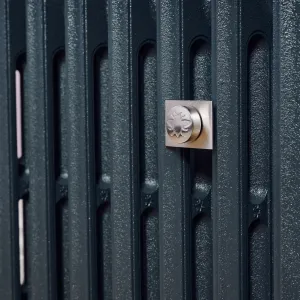 Close-up of a brushed nickel-look Whitworth wall stay with a square backplate and embossed bee cap on a textured Anthracite Grace radiator.