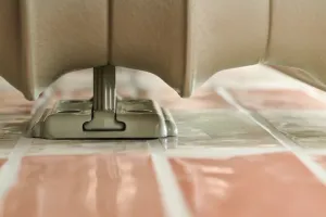 Close-up of the base of an Emmeline I cast iron radiator in Pebble Grey, showing a slim foot and floor plate on pink glazed tiles.