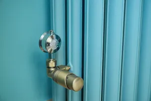 Close-up of an Emmeline III cast iron radiator in teal blue with an antique brass thermostatic valve and chrome air vent against a matching wall.