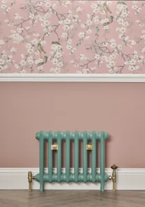 Low Emmeline I cast iron radiator in green Little Greene Pleat 280 on feet, brass valves, below a pink wall with blossom wallpaper.