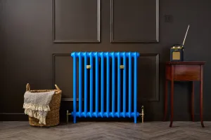 Emmeline I 865mm cast iron radiator in Benjamin Moore Evening Blue 2066-20 with brass valves, against a dark panelled wall beside a wicker basket.