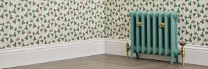 Emmeline I cast iron radiator in Little Greene Pleat 280 on feet, with brass valves and wall stays, against floral wallpaper on a herringbone floor.