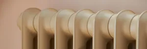Close-up of the rounded top sections of an Emmeline I cast iron radiator in a pale beige finish against a soft pink wall.