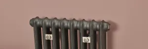Top of a plain cast iron column radiator in Black Iron with two wall stays, set against a dusky pink wall.