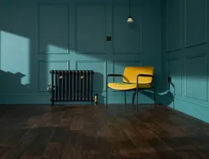 Emmeline I cast iron radiator in Midnight Ink with brass valves and wall stays, beside a yellow armchair in a teal panelled room.