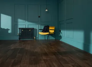 Emmeline I cast iron radiator in Midnight Ink on feet with brass valves, in a teal panelled room beside a yellow chair on dark wood floor.