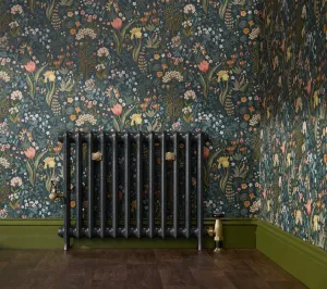 Emmeline I cast iron radiator in Midnight Ink on feet with brass wall stays and valves, against floral wallpaper and a green skirting board.