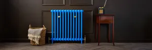 Emmeline I cast iron radiator in bright blue Evening Blue with brass valves, against a dark panelled wall on a herringbone floor.