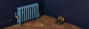 A low cast iron radiator painted mid blue on feet, with brass valves and wall stays, in a navy room with parquet floor and boots in the corner.