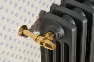 Close-up of a Grace 4 Column cast iron radiator in dark grey Pencil with a Natural Brass angled valve, against blue star-patterned wallpaper.