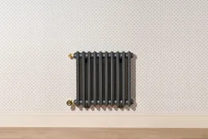 Wall-hung Grace 4 Column 660mm cast iron radiator in dark grey with brass valves, on dotted wallpaper above a skirting board and wood floor.