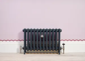 Grace 4 Column 500mm cast iron radiator in Anthracite on feet, with nickel valves, against a pink wall with a scalloped red border.