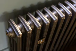Close-up of a plain Grace 4 Column cast iron radiator in a burnished silver-grey metal finish, with a brass end plug and wall stay.