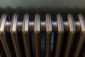 Close-up along the top of a plain Grace 4 Column cast iron radiator in Beaten Brass, showing its rounded sections and joining necks.