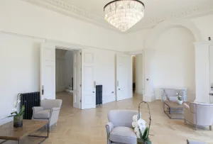 Two Grace 4 Column cast iron radiators in Astral Grey Dark beside panelled double doors in a cream room with herringbone oak floor and armchairs.