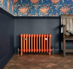 Orange Grace 6 Column cast iron radiator on feet with nickel valves, below navy panelling and floral wallpaper, beside a wooden chair.
