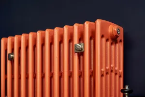 Close-up of a plain Grace 6 column cast iron radiator in bright orange against a navy wall, with a satin nickel wall stay and valve.