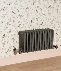 Wall-hung Grace 6 Column cast iron radiator in Quartz Grey with Chatsworth angled valves, against bird-print wallpaper above a pink skirting board.