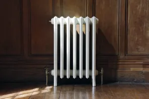 Grace 6 Column 660mm cast iron radiator in white on feet, with brass angled valves, against oak panelling on a wooden floor.