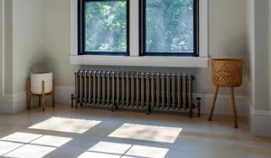 Grace 4 column cast iron radiator in Grey Bronze on feet beneath a window, with angled valves, a light oak floor and plant stands either side.