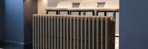 Grace 6 Column cast iron radiator in a bronze-toned metallic finish, freestanding in front of three upholstered bar stools.