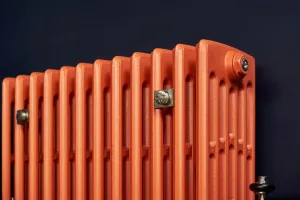 Close-up of a plain Grace 6 column cast iron radiator in Benjamin Moore Fireball Orange 2170-10 with nickel wall stays against a navy wall.