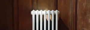 Top of a white Grace 6 Column 660mm cast iron radiator, wall-hung against dark oak panelling in raking sunlight.