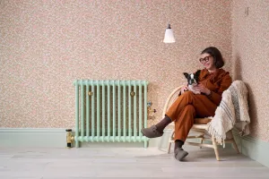 Plain Mercury 2 Column cast iron radiator in Little Greene Pea Green 91 with brass valves, beside a woman and dog on a rattan chair.