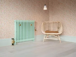 Plain Mercury cast iron column radiator in Pea Green 91 with brass valves and wall stays, beside a rattan chair against floral wallpaper.