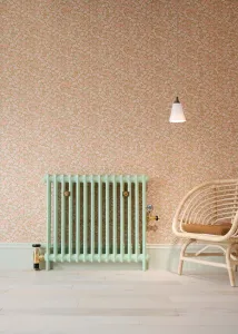 Plain Mercury 2 column radiator in Pea Green 91 on feet, with brass valves and stays, against floral pink wallpaper beside a rattan chair.