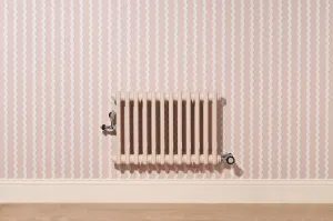 Plain wall-hung Mercury 3 Column 560mm radiator in Farrow & Ball Scallop No. 311 with chrome valves, on pink wavy-striped wallpaper above a skirting board.