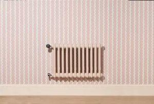Wall-hung plain Mercury 3 Column cast iron radiator in Farrow & Ball Scallop No. 311 with chrome valves, on pink wavy-striped wallpaper.
