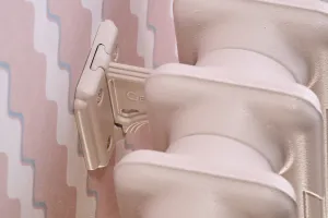 Close-up of a cast iron wall stay holding a plain Mercury radiator in pale pink Scallop No. 311, against pink zigzag wallpaper.