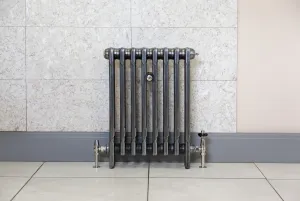 Mercury 3 Column 660mm cast iron radiator in a metallic graphite finish on feet, with nickel valves, against a marble-effect wall and tiled floor.