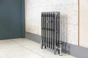 Plain Mercury 3 column cast iron radiator on feet in a burnished metal finish, with a nickel valve, against a marble-effect wall on a tiled floor.