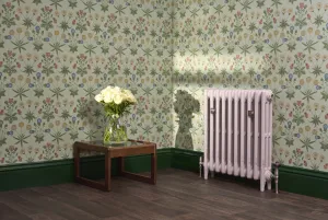 Plain Mercury 3 column cast iron radiator on feet in Dorcester Pink, with satin nickel Windsor valves, against floral wallpaper and green skirting.