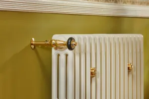 Close-up of a plain Mercury 3 Column cast iron radiator in Farrow & Ball Lime White No. 1 with a polished brass Windsor valve on an olive wall.