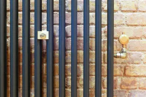 Close-up of a Mercury 3 Column cast iron radiator in Matt Black against exposed brick, with a brass wall stay and brass angled valve.